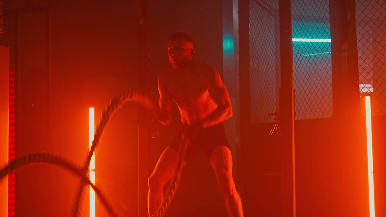 Homem Atlético Treinando com Cordas Navais em Academia Iluminada por Neon