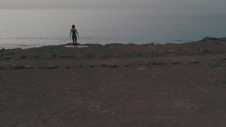 mujer practicando yoga en una playa al amanecer o al atardecer