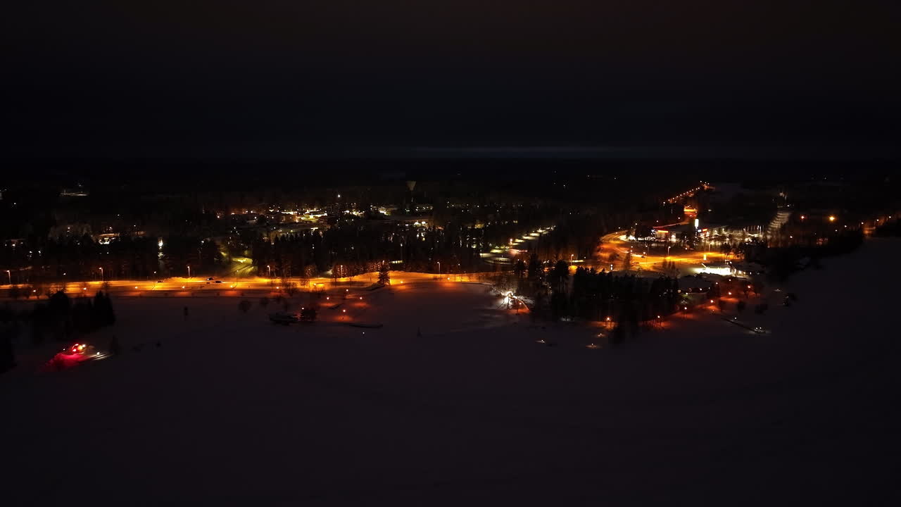 vista aérea acercándose a la iluminada ciudad de suomussalmi, noche de invierno en finlandia