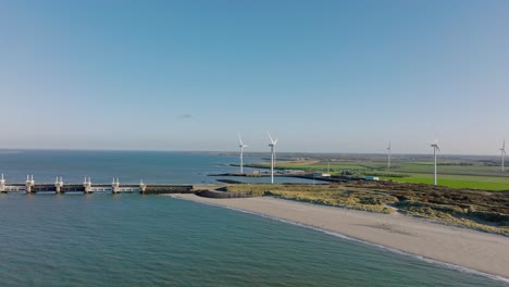 Toma-Aérea-En-Cámara-Lenta-De-Turbinas-Eólicas-Y-La-Barrera-Contra-La-Marejada-Ciclónica-De-Scheldt-Oriental-En-Zelanda,-Los-Países-Bajos-En-Un-Hermoso-Día-Soleado