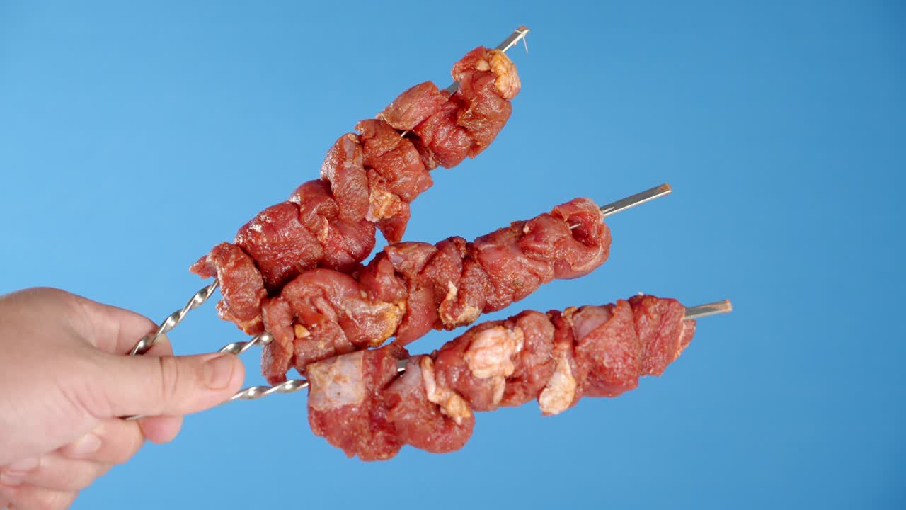 The men's hand holds a skewer with raw pork kebab.