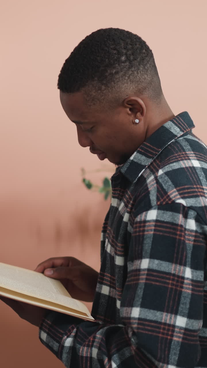 Man reads book standing next to shelf. Thoughtful dark-skinned bookworm dips into literature standing in premise of college library. Reading as hobby
