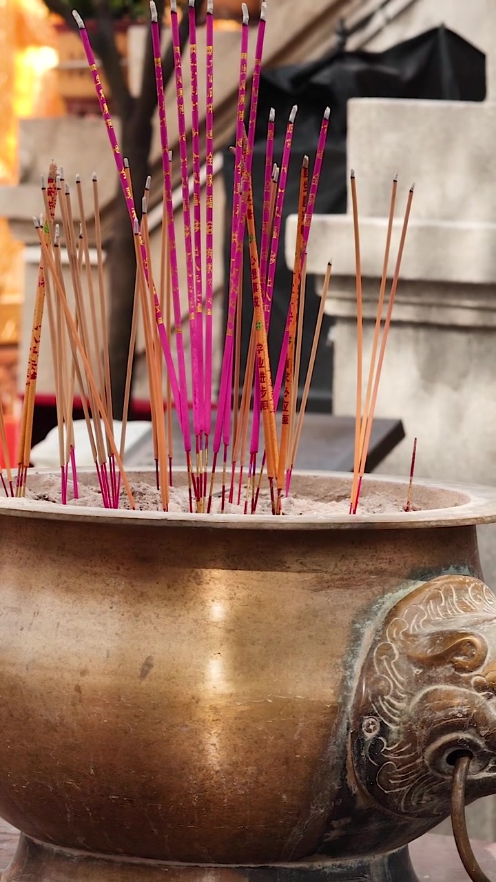 Un gros plan vertical de bâtonnets d'encens roses se consumant dans un brûleur en laiton orné.