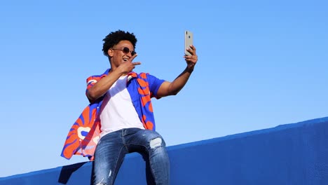 smiling black man taking selfie while siting on fence