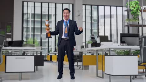 full body of asian business man in a suit and tie with a gold medal and trophy screaming goal celebrating winning as the first winner in office
