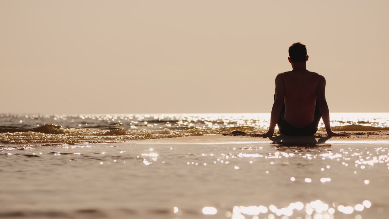 작은 모래섬에 앉아 있는 청년의 실루엣
