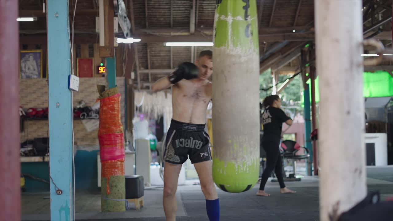 Man training Muay Thai with a heavy bag in a gym
