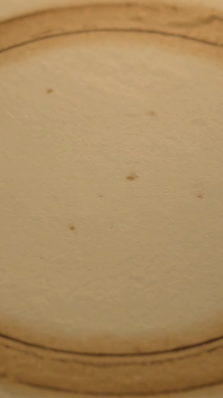 Vertikal video: Bevægeligt kamera filmer en rund skål på et bord, der viser kantbuer og en beige-plettet inderside.