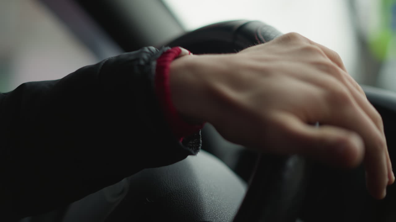 Close up shot of male driver placing hand on steering wheel, rotating wheel smoothly with practiced motion, focus on wrist and fingers gripping leather wheel as urban road scene blurs outside window