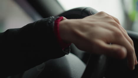 close up shot of male driver placing hand on steering wheel, rotating wheel smoothly with practiced motion, focus on wrist and fingers gripping leather wheel as urban road scene blurs outside window