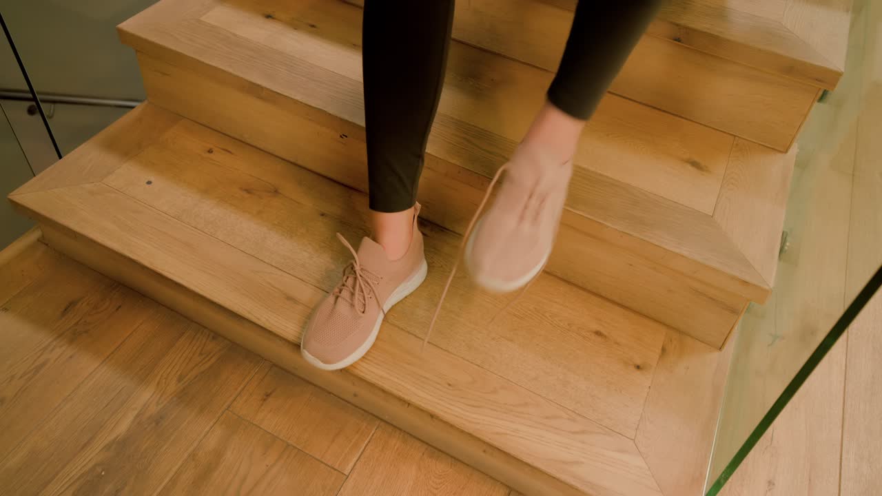 Adult woman stepping down into wooden stairwell, sitting and tying sneaker laces before leaving