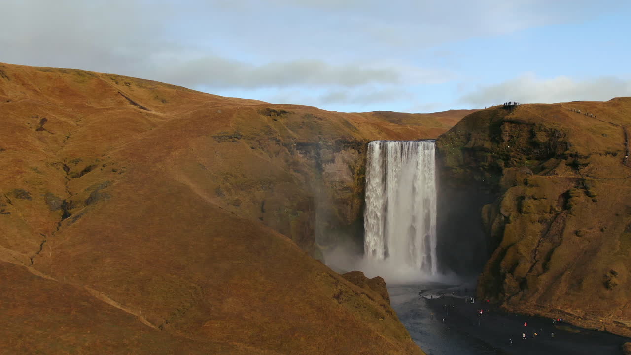 avión no tripulado cinematográfico cascada de skogafoss islandia pan hacia abajo movimiento con pájaros, arco iris y luz del sol de la tarde