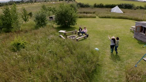 Drone-Shot-Of-Group-Of-Mature-Friends-Sitting-Around-Camp-Fire-On-Yurt-Campsite