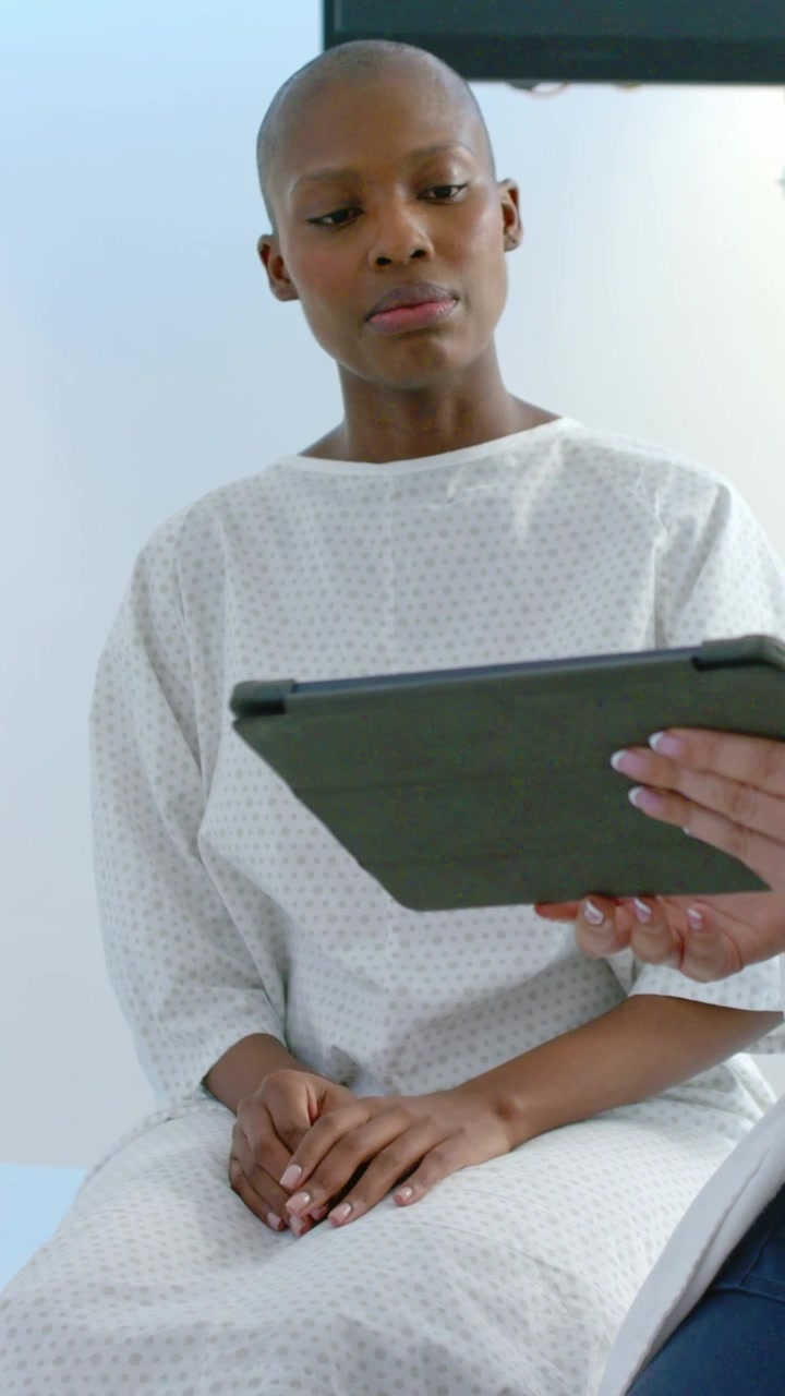 Vertical video: Watching patient in gown reading tablet held by clinician in exam room, thinking
