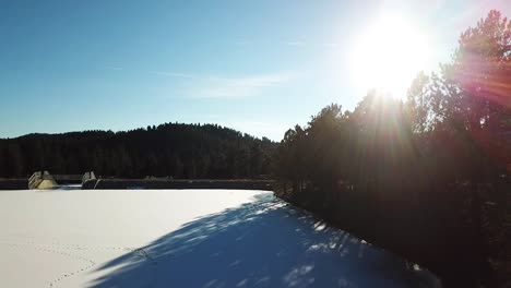 Sun-coming-through-trees-in-Colorado-mountain-over-frozen-lake