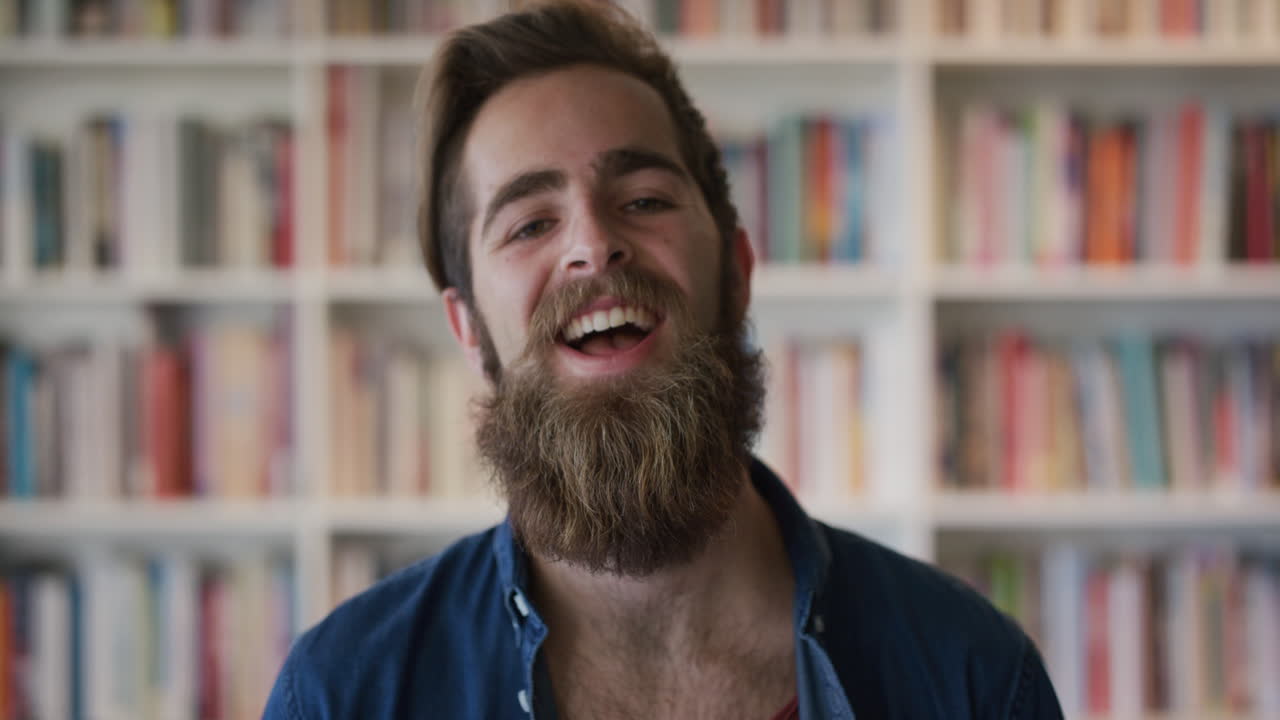 portrait cute bearded hipster man student laughing enjoying successful college education lifestyle happy entrepreneur in bookshelf background slow motion