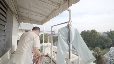 asian man on his apartment balcony hanging up freshly washed clothes to dry - slow motion