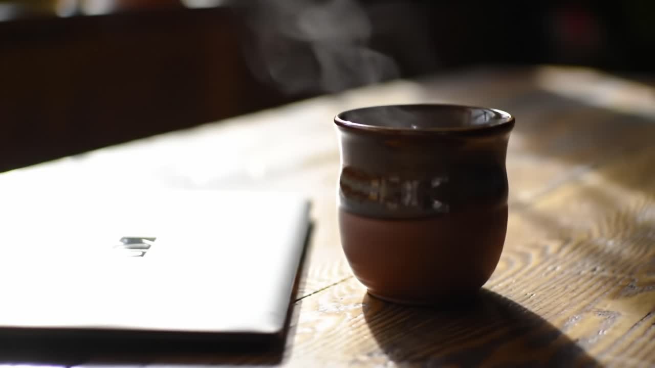 A Serene Morning Ritual: Enjoying a Hot Beverage Next to a Laptop on a Rustic Wooden Table Surrounded by Soft, Natural Light