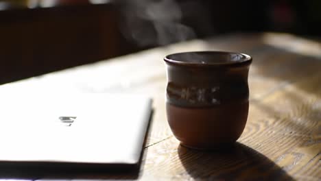 a serene morning ritual: enjoying a hot beverage next to a laptop on a rustic wooden table surrounded by soft, natural light