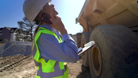 Extreme-closeup-wide-angle-view-of-female-architect,-engineer,-project-manager-on-a-construction-site-talking-on-a-smartphone-and-using-a-tablet-computer-and-clipboard