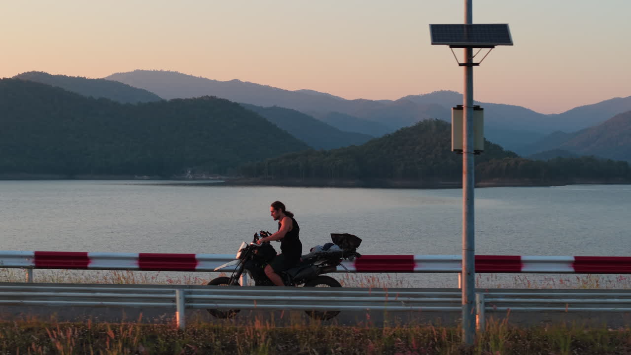 日の出時、湖のほとりをバイクで走る男性