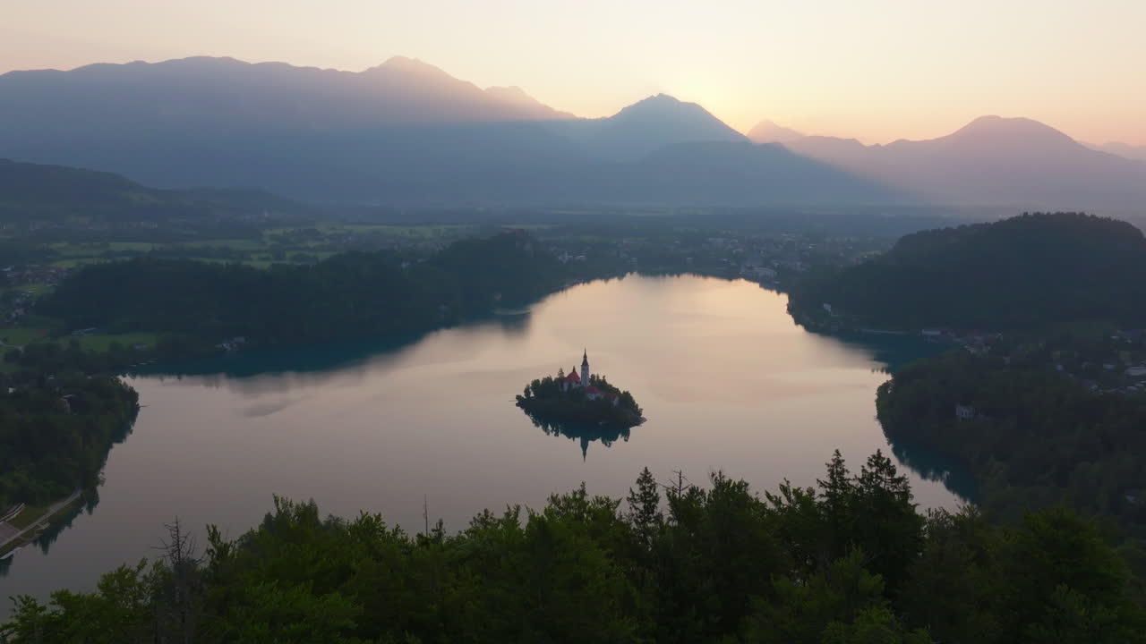 Drone video of Lake Bled, Slovenia at golden sunrise with calm water and island