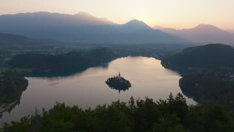 Drone video of Lake Bled, Slovenia at golden sunrise with calm water and island