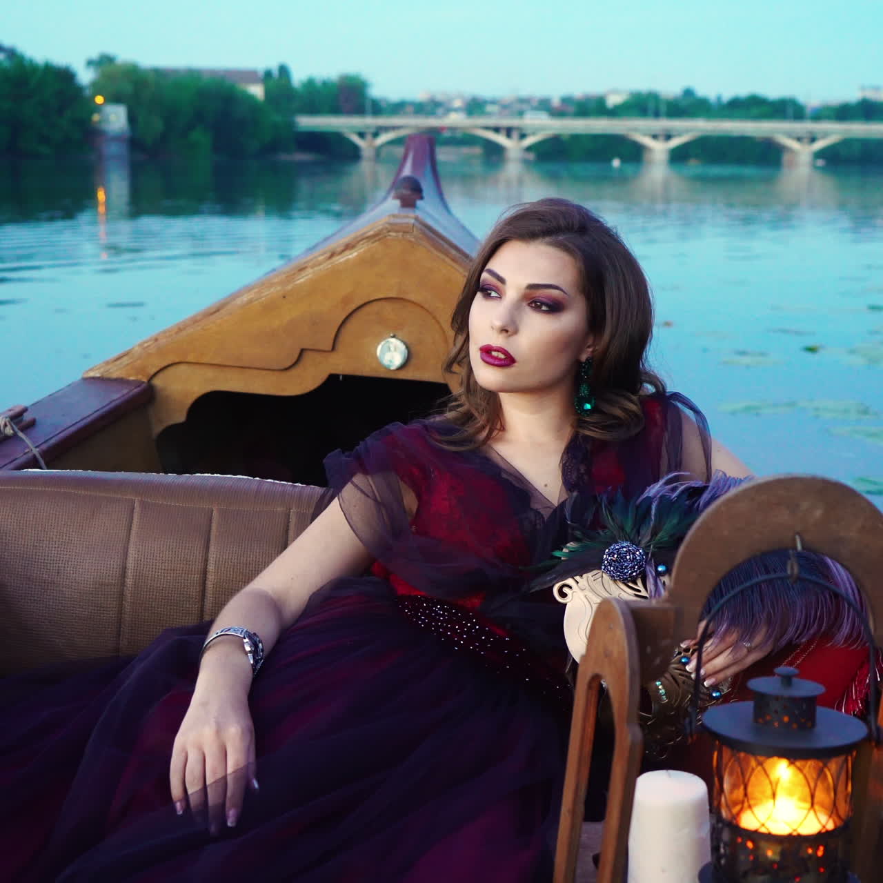 Elegant female with perfect make-up and beautiful dress riding a boat on the background of a bridge over the river. Pretty young lady floating in gondola in the evening
