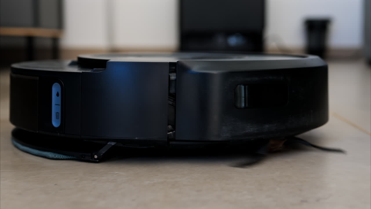 Close up of a black robot vacuum cleaner moving and rotating on the floor tiles