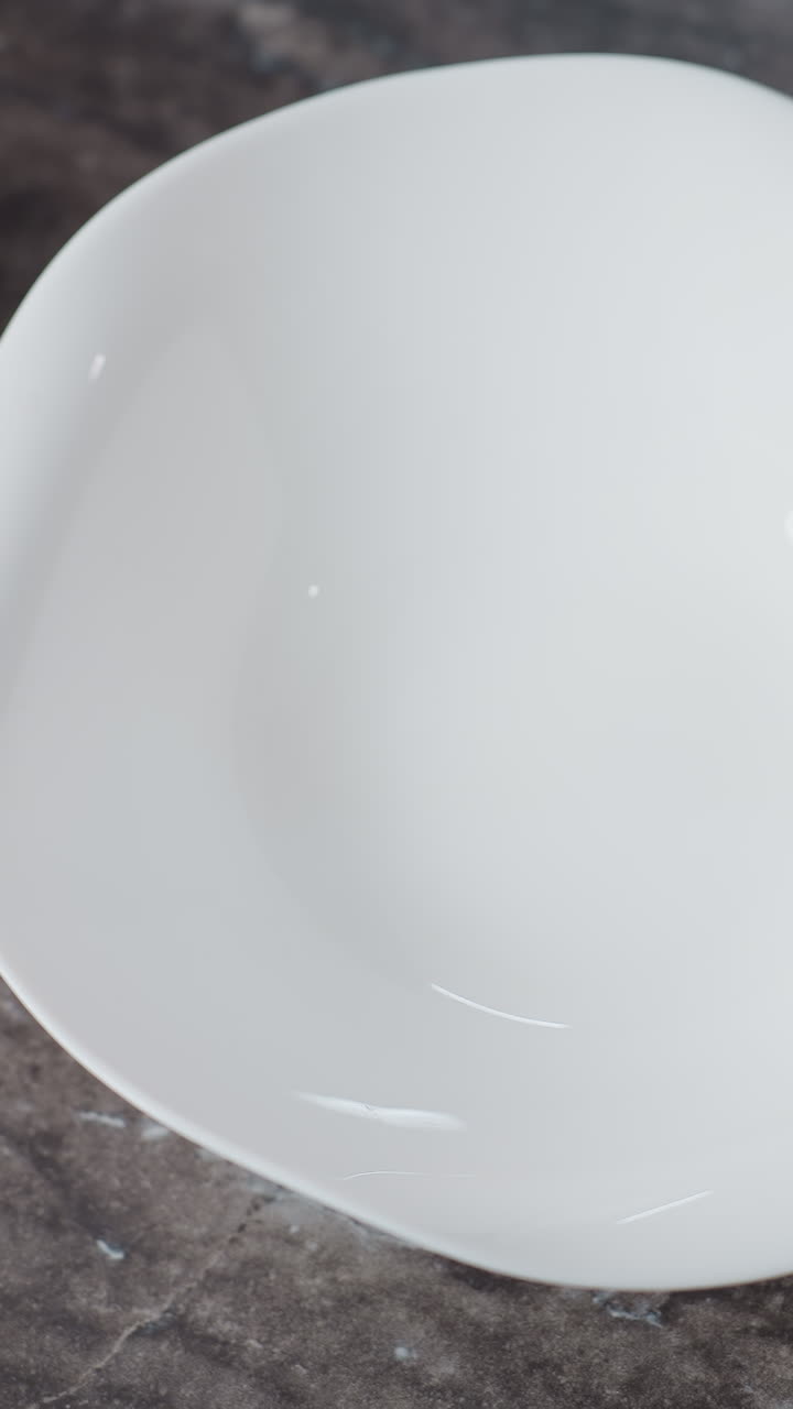 Aerial view of chef hand placing white bowl on kitchen table, gently dropping eggs while wearing a bracelet, red burning candle and glass cup of sugar on countertop