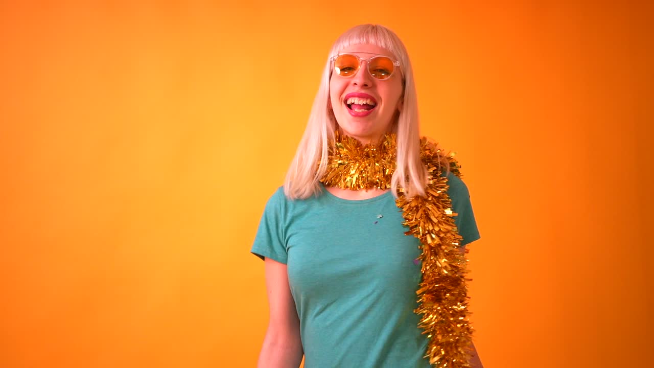 Woman celebrating with confetti and tinsel on orange background