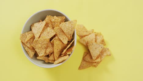 close up of nachos falling in a bowl on yellow surface