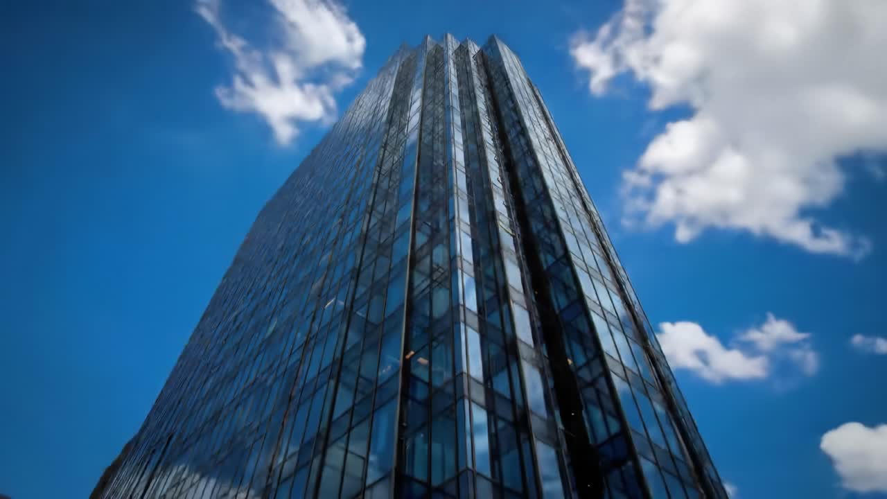 A sleek skyscraper towers upward, showcasing its glass façade reflecting the clouds above. The architecture stands out in the bustling cityscape, highlighting modern design.