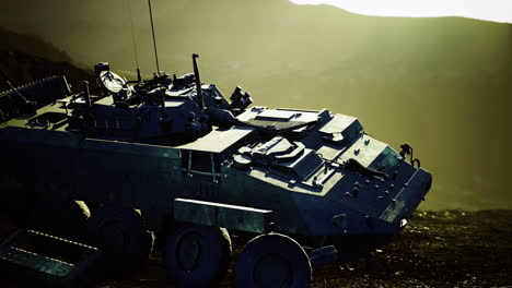 a robust armored vehicle rests on rocky ground silhouetted by a glowing sunset