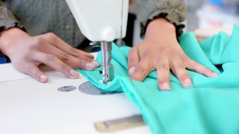 Diseñadora-De-Moda-Birracial-Cosiendo-Tela-Con-Máquina-De-Coser-En-Estudio,-Cámara-Lenta