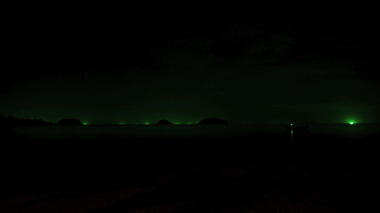 ночной таймлапс во время грозы с молниями на таиландском пляже на острове ко чанг, вдалеке видны зеленые огни рыбацких лодок