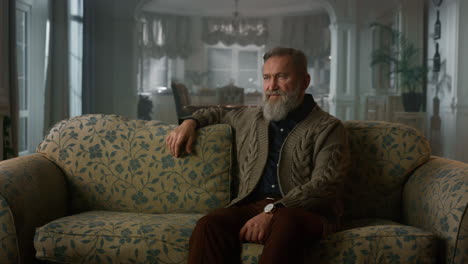 handsome senior man thinking while sitting in the sofa in cozy living room