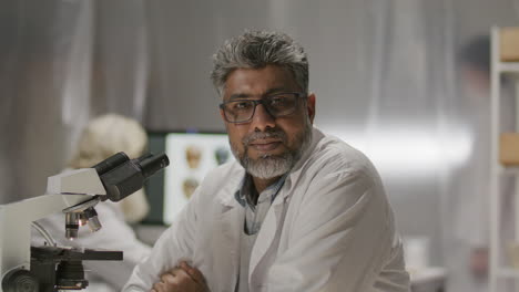 portrait of confident mature scientist at laboratory table with microscope