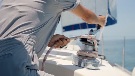 close up of female hands wind up rope on sailboat's winch on sunny day. full frame slow motion