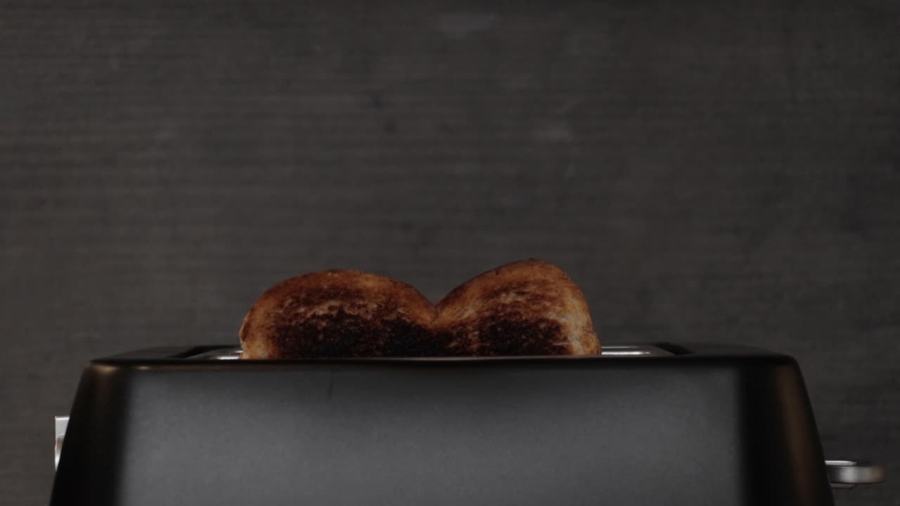 A shot of some burnt toast popping out of a black matte toaster with smoke rising from it