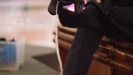 una vista de cerca de alguien tirando de un zapato de patinaje sobre hielo negro con un zapata de patinajes azul visible en un recipiente transparente
