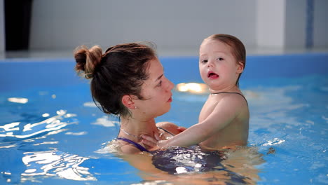 beautiful mother teaching cute baby girl how to swim in a swimming pool. child having fun in water with mom.