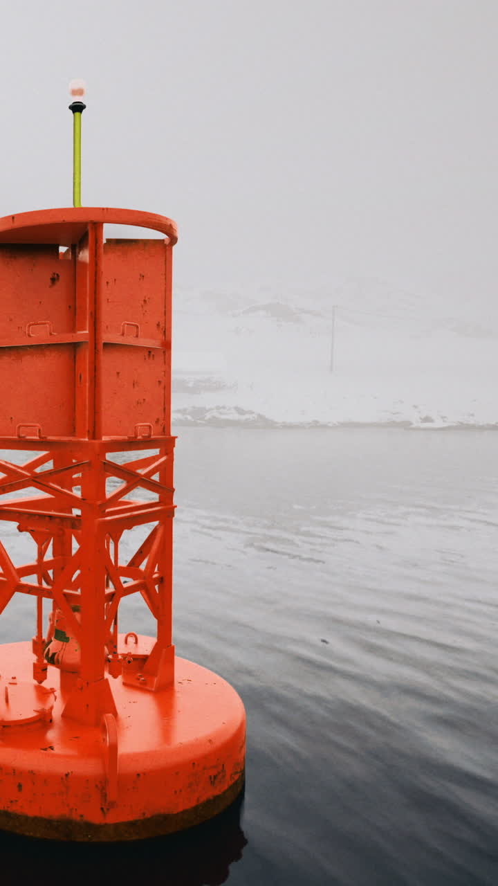 Bright orange buoy in calm water near snowy landscape during cloudy weather