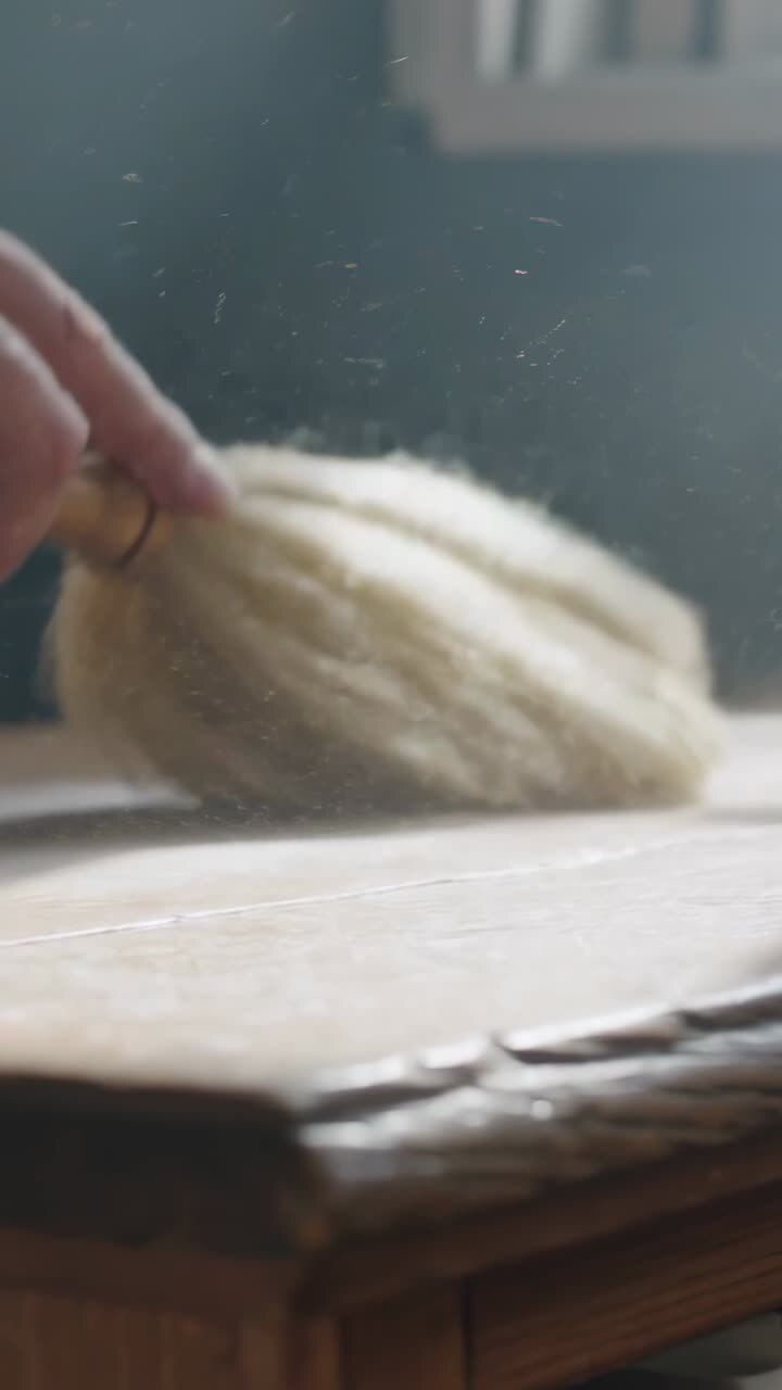Vertical video: Entering hand moving cream fiber on cardboard by window, revealing gold ring, dust