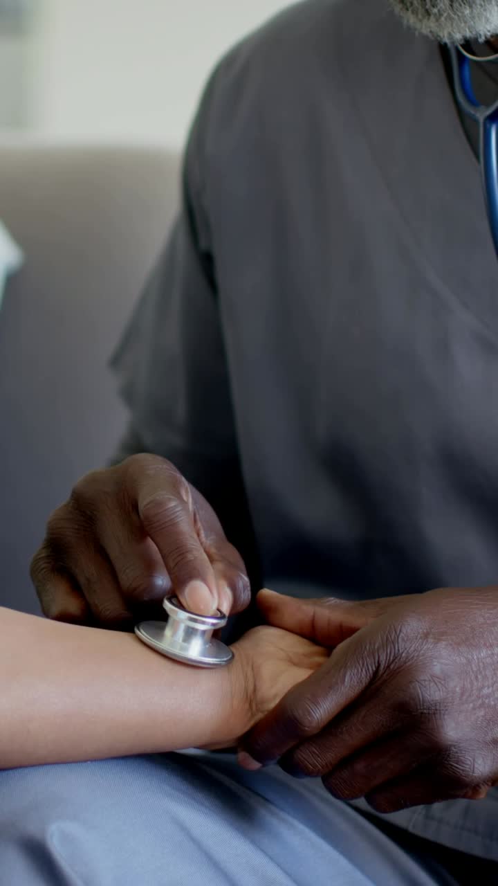 Video verticale: Uomo in divisa medica grigia che posiziona uno stetoscopio blu e controlla il polso al polso, usandolo sul divano.