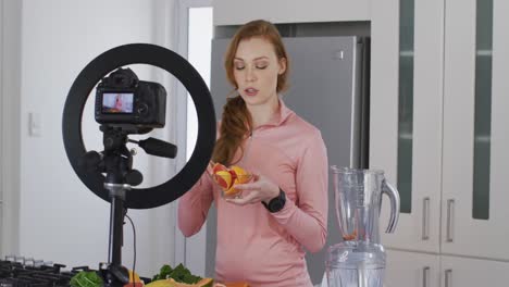 mujer sosteniendo un plato de fruta picada y grabándola con cámara digital en la cocina