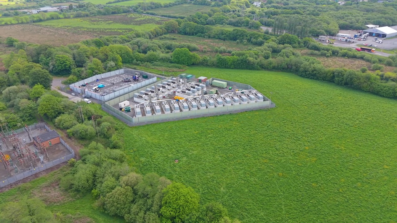 Wide Orbiting Aerial of Modern Gas Peaking Plant with exhaust stacks, generators, cooling systems. Provides rapid-response electricity to the grid during peak demand. Energy infrastructure. UK.