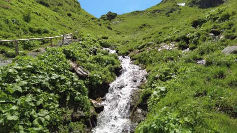 small waterfall next to a hiking trail in a green mountain landscape