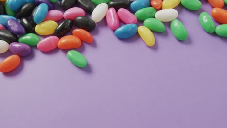 Video-of-close-up-of-multi-coloured-sweets-with-copy-space-over-purple-background