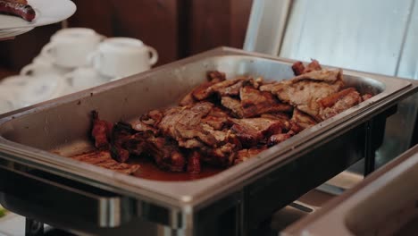 steaming grilled pork and sausages in tray being served at buffet table